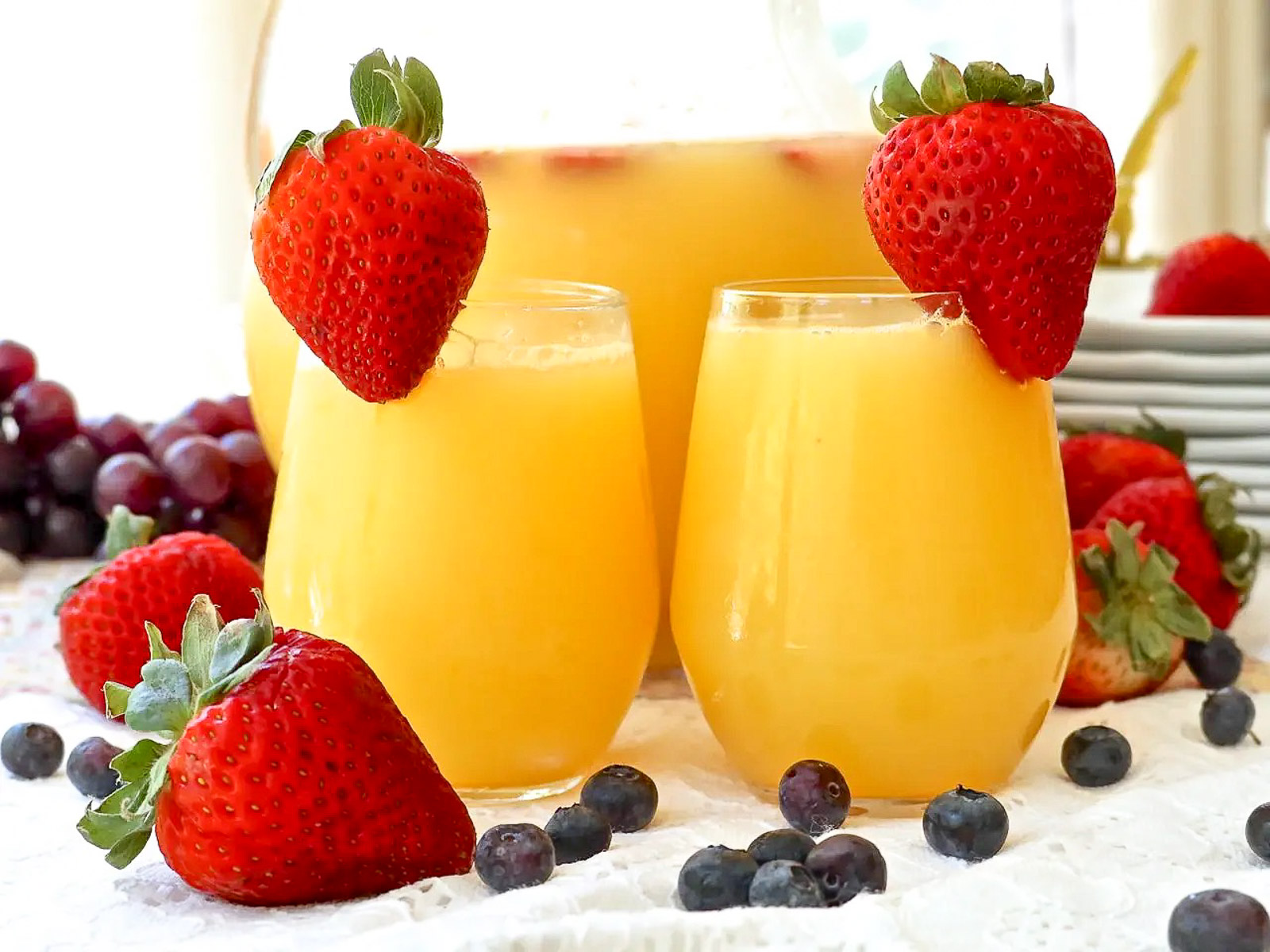 Brunch menu ideas: fresh mimosa in a pitcher and served in glasses. Garnished with strawberries