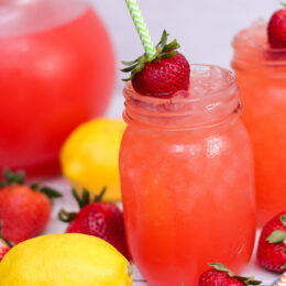 Ice cold glass of strawberry lemonade with a straw and strawberry garnish