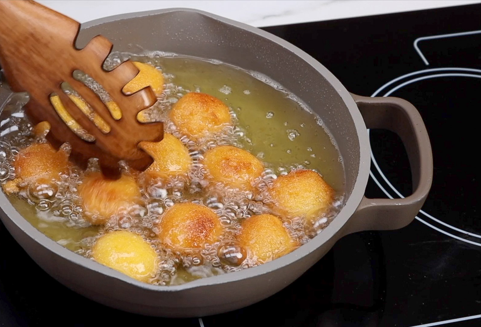 Golden brown homemade Southern buttermilk hush puppies frying in oil.