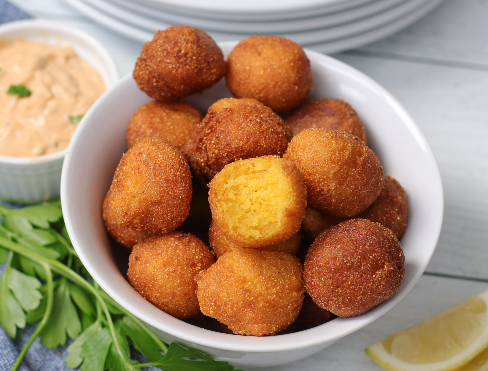 golden, crisp hush puppies in a bowl showing fluffy inside texture.