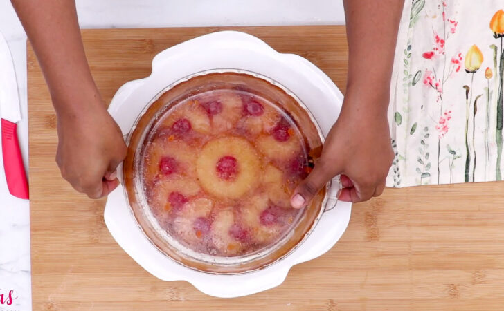 Lifting pan off of pineapple upside-down cake after inverting it.