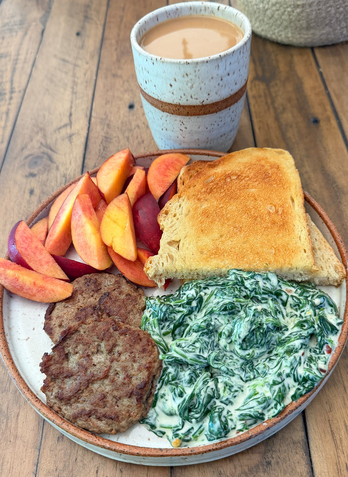 Healthy breakfast plate of creamed spinach, turkey sausage, sliced peaches and sour dough bread.
