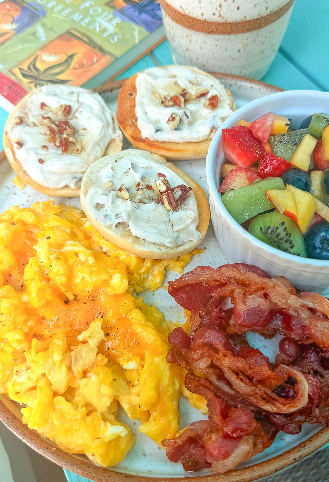 Quick breakfast idea featuring a mini bagel with cream cheese, fresh fruit, scrambled eggs and beef bacon